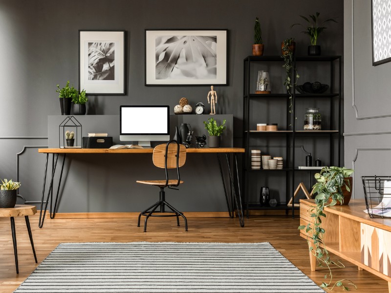 Schreibtisch vor grauer Wand. Der Holzfußboden schenkt dem Raum Wärme und Behaglichkeit